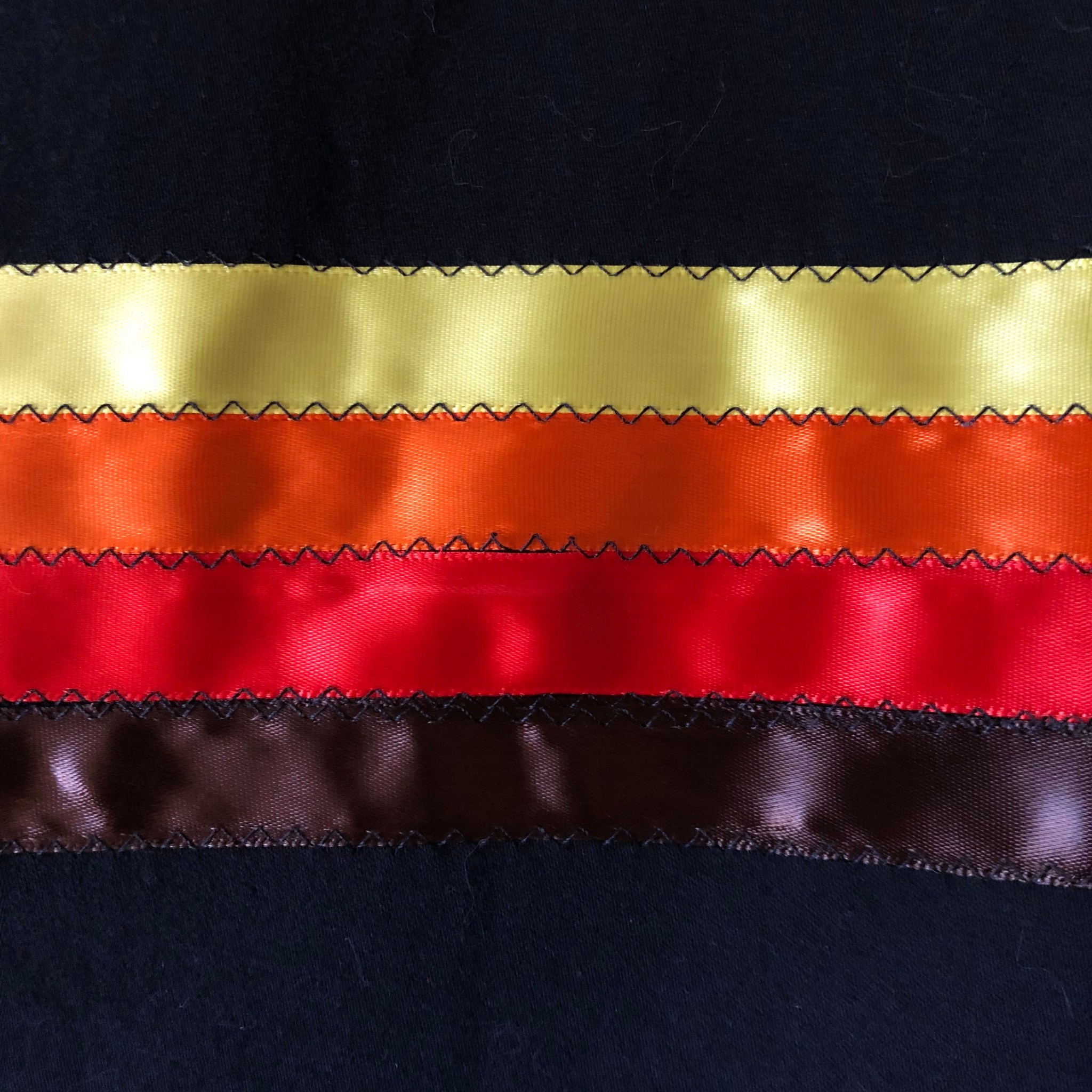 A photo of black, yellow, orange, and red ribbons sewn together