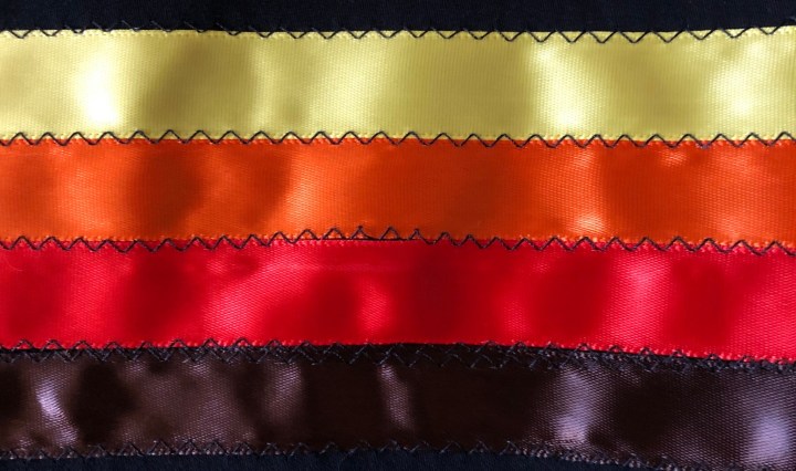 A photo of black, yellow, orange, and red ribbons sewn together
