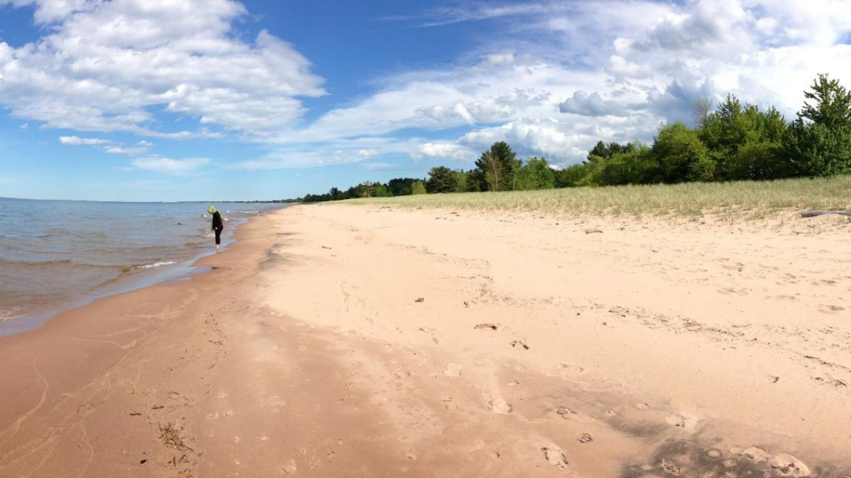 A beach next to Lake Superior on a sunny day. In the distance, a person is wading in the water.